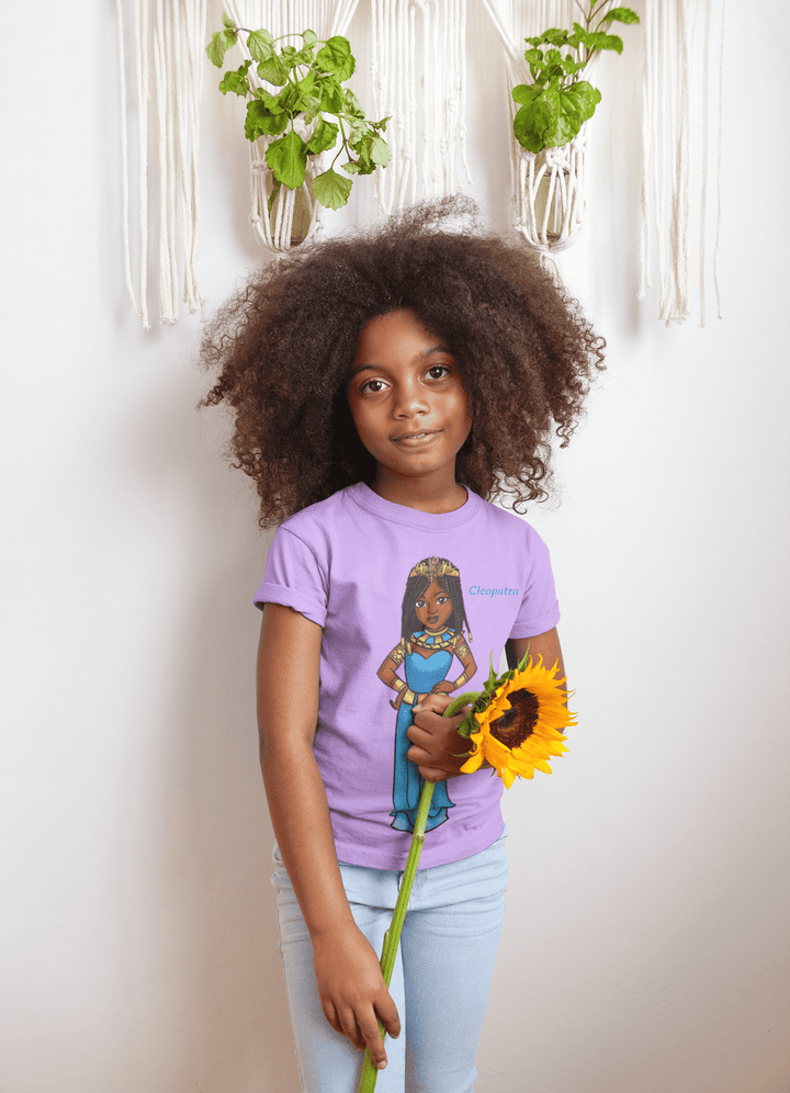Young Black girl wearing a lavender Cleopatra T-shirt from TL Johnson Stories, holding a sunflower. The shirts represent cultural empowerment fashion for children.