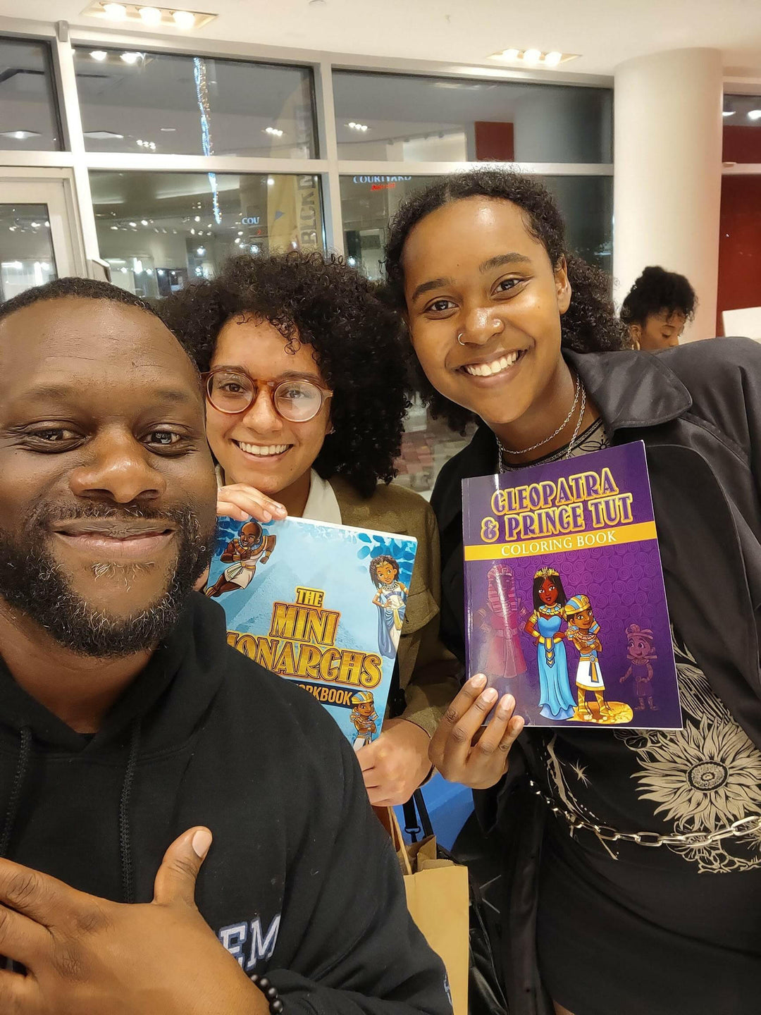 Cleopatra & Prince Tut Coloring Book. being held up at an event also next to the mini monarchs activity book. 